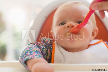 Close up cute baby girl being fed by spoon in high chair