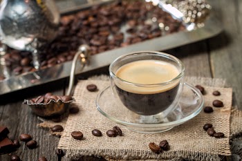 Close up espresso glass cup with coffee bean, chocolate and creamer on old wooden table
