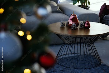 Close up of modern small round wooden table with beautiful decoration near cozy grey sofa and near Christmas tree. Concept of modern fashionable interior with Christmas decoration.