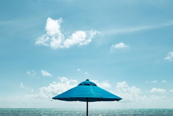 Close-up Photo of Blue Parasol Near Body of Water Under Blue Sky