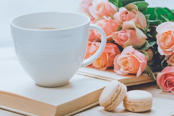 Close-Up Photo of Coffee Mug Near Pink Roses and Macarons