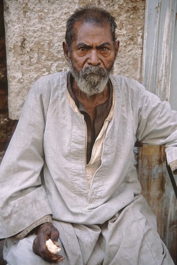 Close-up Photo of Elderly Man in Beige Thobe Sitting Alone by Wall