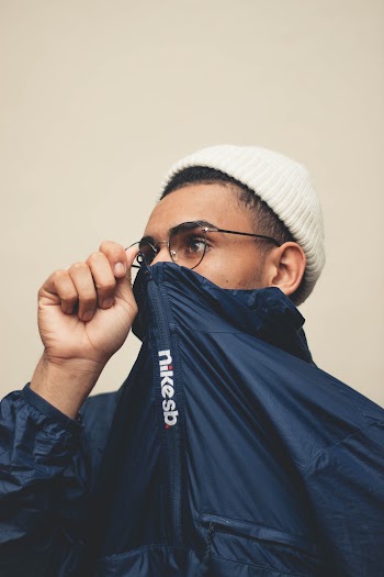 Close-up Photo of Man in Beanie Hat and Glasses Covering His Mouth With His Blue Jacket