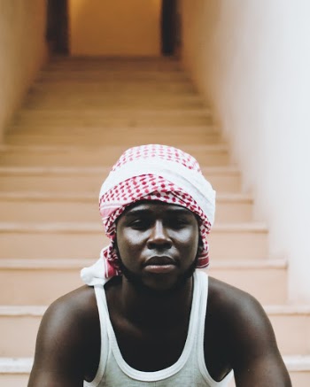 Close-up Photo of Man in White Tank Top and Keffiyeh Headband Sitting on Stairs
