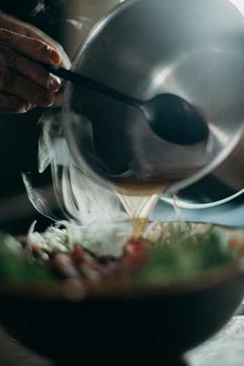 Close-Up Photo of Person's Hand Pouring Soup From Stainless Bowl