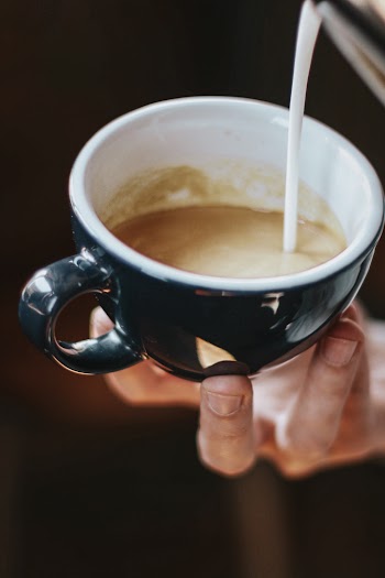 Close-Up Photo of Person Pouring Milk On Cup
