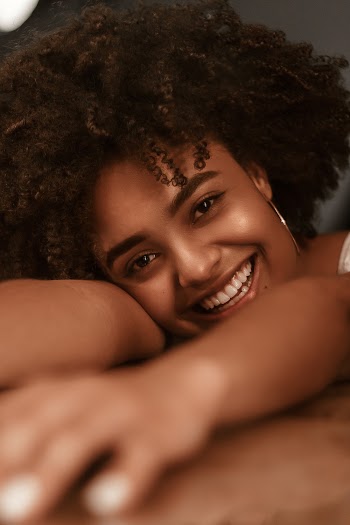Close-up Photo of Smiling Woman Resting Her Head ans Hands on Wooden Surface