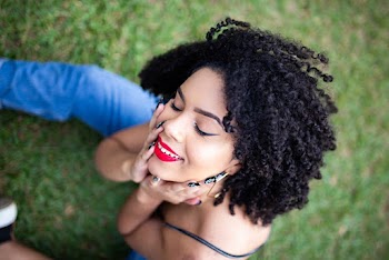 Close-up Photo of Smiling Woman Sitting on Grass Posing with Her Eyes Closed