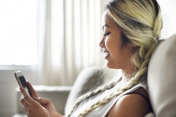 Close-up Photo of Smiling Woman Sitting on Sofa Using Smartphone