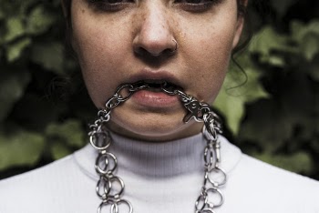 Close-up Photo of Woman's Face Posing While Biting a Silver Chain Necklace