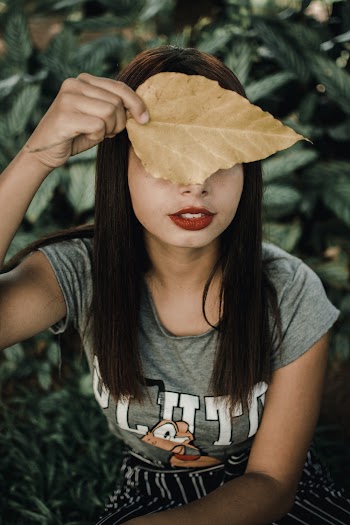 Close-up Photo of Woman in Grey T-shirt Covering Her Face With a Brown Leaf