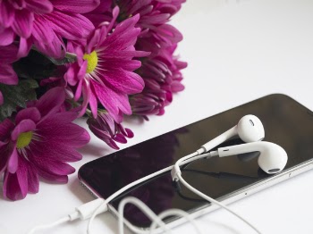 Close-Up Photography of Earphones on Top of Iphone 6 Near Flowers