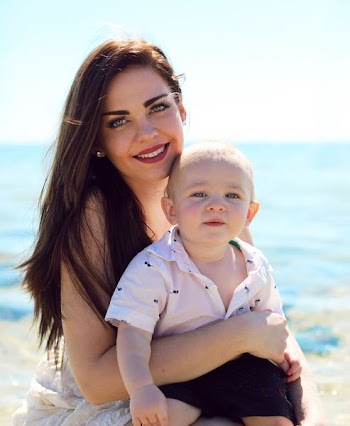 close-up photography of woman carrying a baby behind sea at daytime