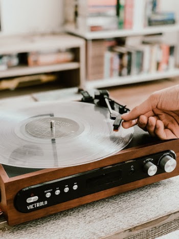 Close up shot of a modern wooden record player playing a clear white vinyl album. A man's hand is dropping the needle onto the record.