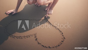 Closeup of hand drawing heart on sand