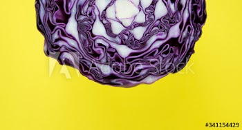Closeup of purple round cabbage cut in half in a yellow background