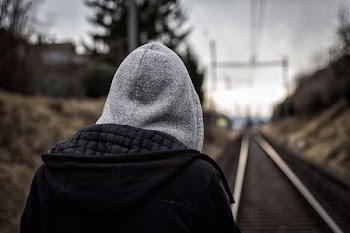 closeup photo of man wearing hoodie in front of train rail