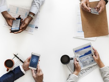 Closeup Photo of Three Persons Hands on Table Holding Smartphones