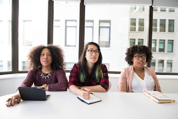 Closeup Photo of Three Women Sit on Chair in Front of Tables