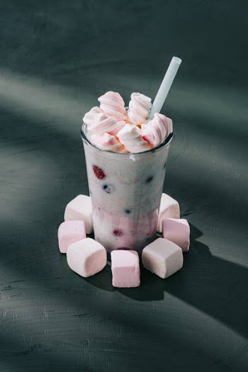 Closeup view of glass with berry smoothie and marshmallows on tabletop