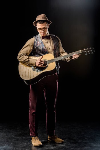 Concentrated young man in stylish hat playing on acoustic guitar on black