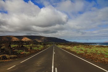 Concrete Road Between Mountain and Body of Water
