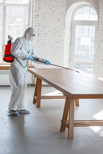 Coronavirus pandemic. a disinfectant in a protective suit and mask sprays disinfectants in the room. Free Photo