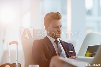 Corporate businessman with suitcase using digital tablet in airport