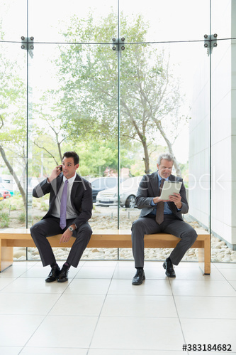 Corporate businessmen with smart phone and digital tablet in modern lobby