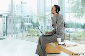 Corporate businesswoman using laptop and smart phone in modern lobby