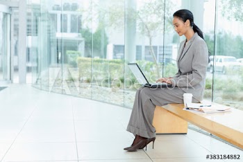 Corporate businesswoman using laptop on bench in modern lobby