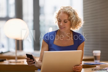 Corporate businesswoman using smart phone at laptop