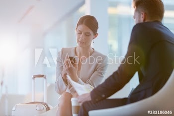 Corporate businesswoman with suitcase using smart phone