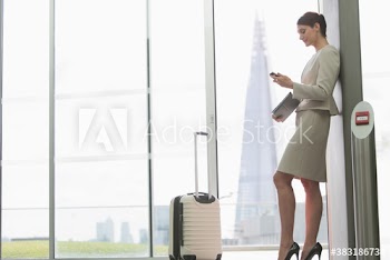 Corporate businesswoman with suitcase using smart phone in city window