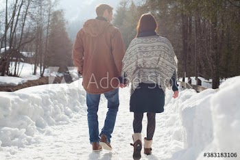 Couple holding hands and walking on sunny snowy footpath