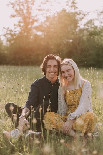 couple sitting on green grass smiling while taking picture
