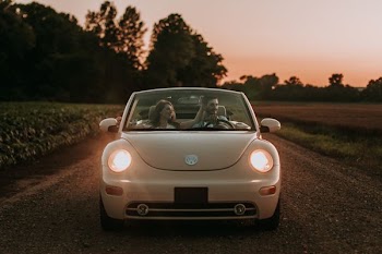 couple sitting on white Volkswagen Beetle convertible coupe on road