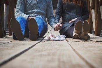 couple sitting on wooden walkway with pair of shoes in between them