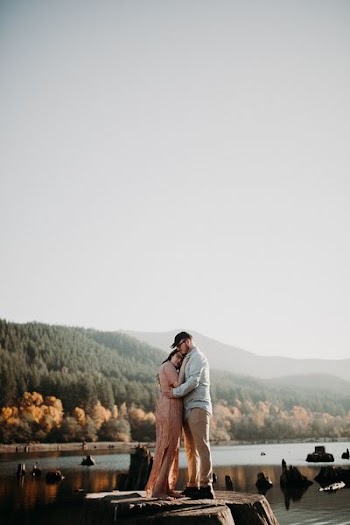 couple standing on formation rock surrounded by body of water during daytime