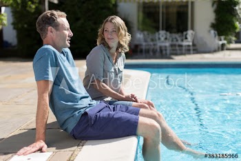 Couple talking and relaxing at sunny swimming pool