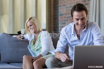 Couple using smart phone and laptop on sofa