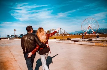couple walking girl pointing red ferris wheel under blue sky and white clouds