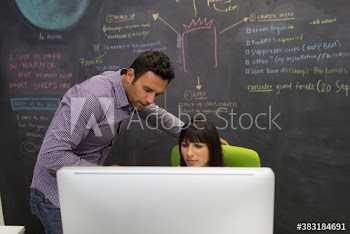 Creative business people working at computer in front of blackboard