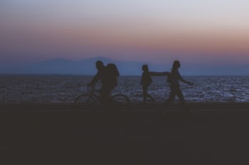 creative unfocused humans wallpaper pattern of fuzzy walking people silhouettes on dark twilight waterfront along Pacific ocean and unfocused mountain horizon background in evening sunset time