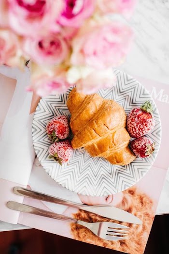 croissant bread and stawberries on beside fork and knife