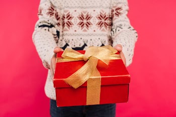 Cropped image of man in sweater showing gift box isolated on pink