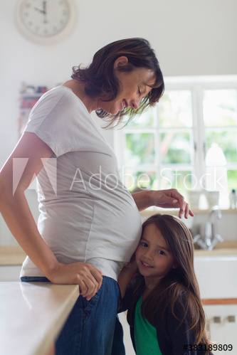 Curious daughter listening to stomach of pregnant mother