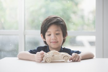 Cute Asian child playing wooden model car on a table
