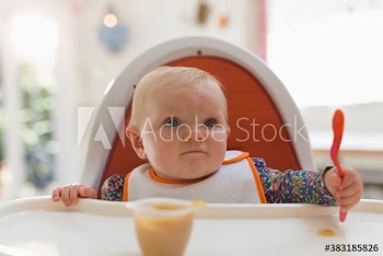 Cute baby girl eating baby food in high chair