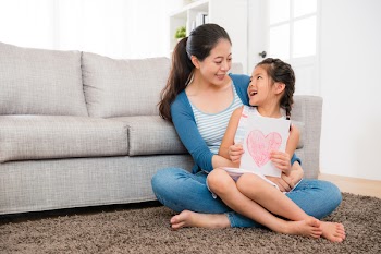 cute little girl prepared mother's day card ready give young woman when sitting on the living room floor together and looking at each other.